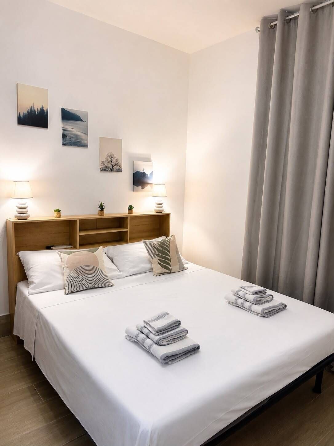 A neatly made bed with pillows and folded towels, a wooden headboard, and wall-mounted artwork.