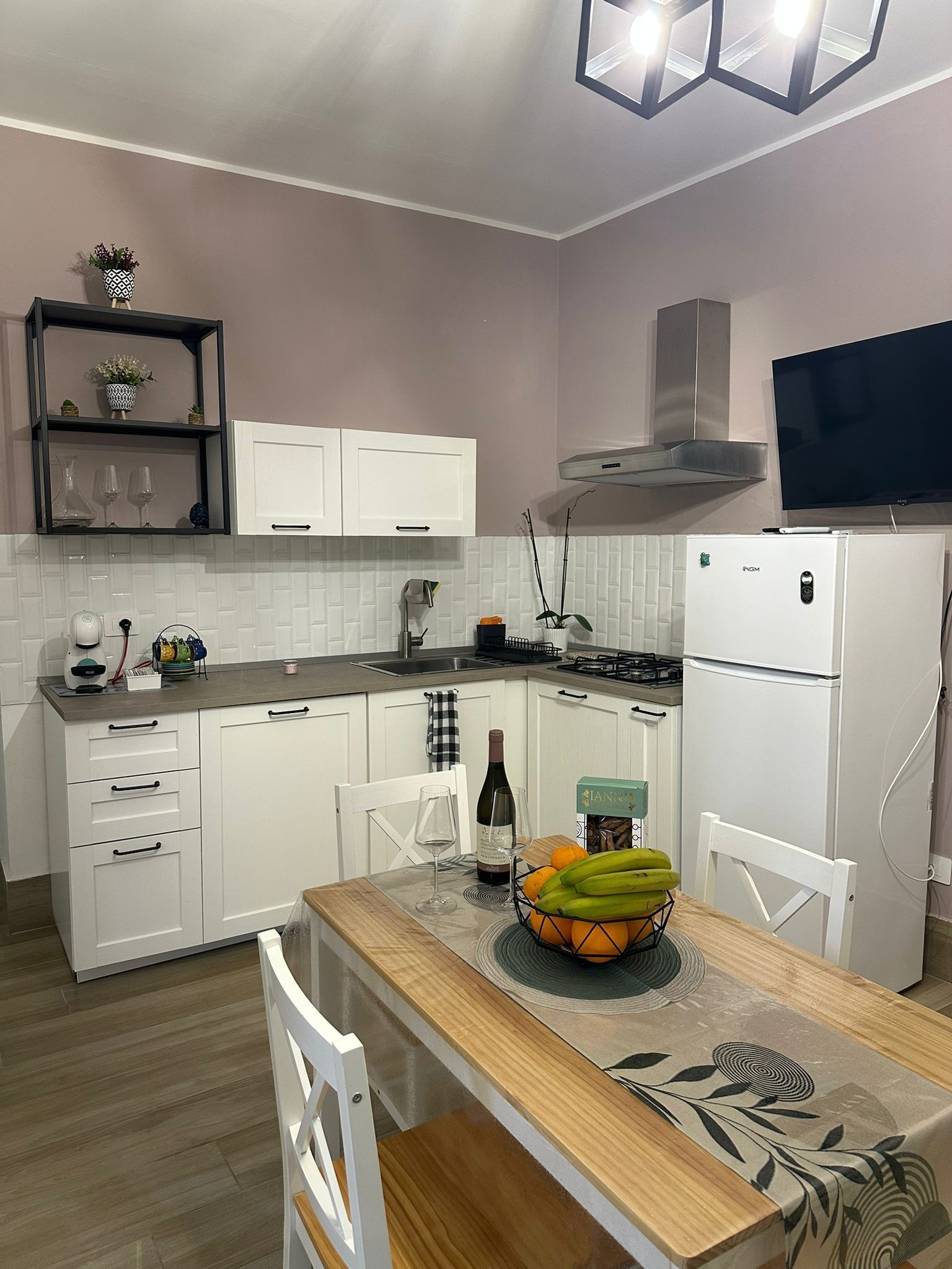 A modern kitchen with white cabinets, a built-in oven, a gas stove, and a TV mounted above the oven.
