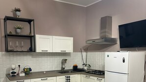 Una cuina moderna amb armaris blancs, forn integrat, fogó a gas i televisió penjada sobre el forn.