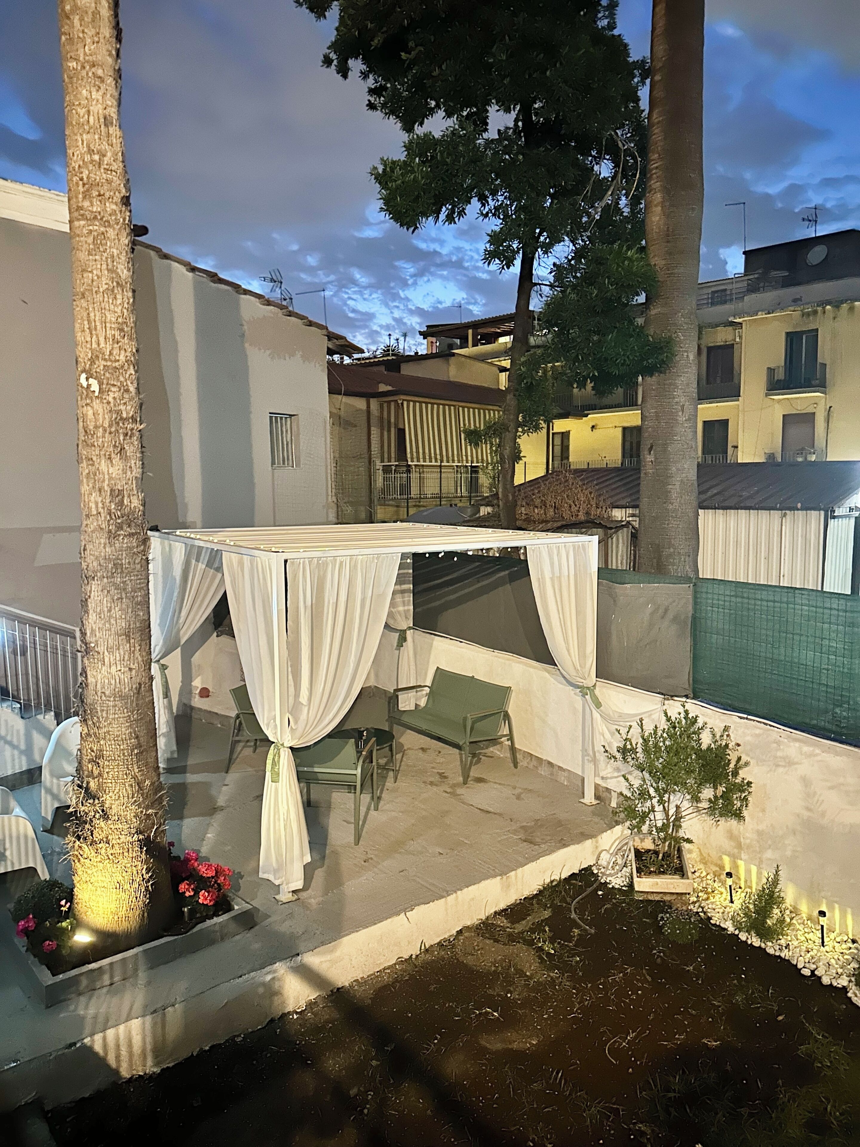 Un patio al aire libre con un área de estar techada, un jardín pequeño y vistas a un edificio al fondo.