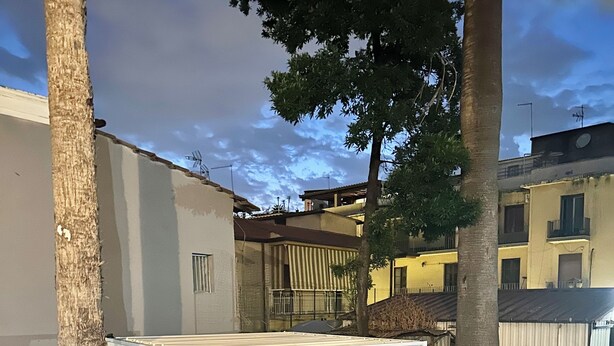 Un pati exterior amb zona de seients coberta, un jardí petit i vista d'un edifici al fons.