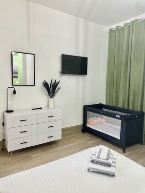 Habitació moderna amb un envellidor blanc, televisió penjada, bressol i llit amb matalàs acolxat.