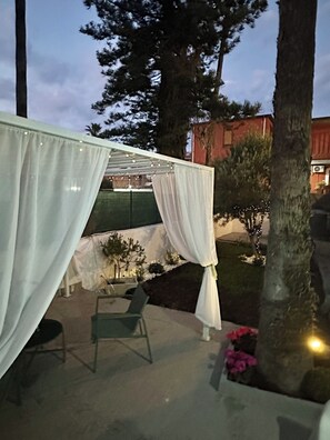 Zona d'estar a l'aire lliure amb un told blanc, una cadira i una taula petita.