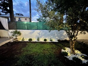 Ein Garten mit Baum, weißen Kieselsteinen und einem grünen Zaun.