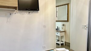 Un dormitori amb un llit, una televisió penjada a la paret, un bany visible per una porta oberta i una tovallola sobre el llit.