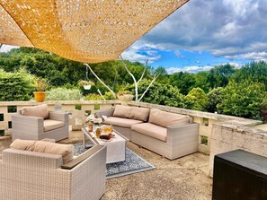 Eine Terrassengruppe im Freien mit Korbmöbeln, einem Tisch mit Getränken und Blick ins Grüne.
