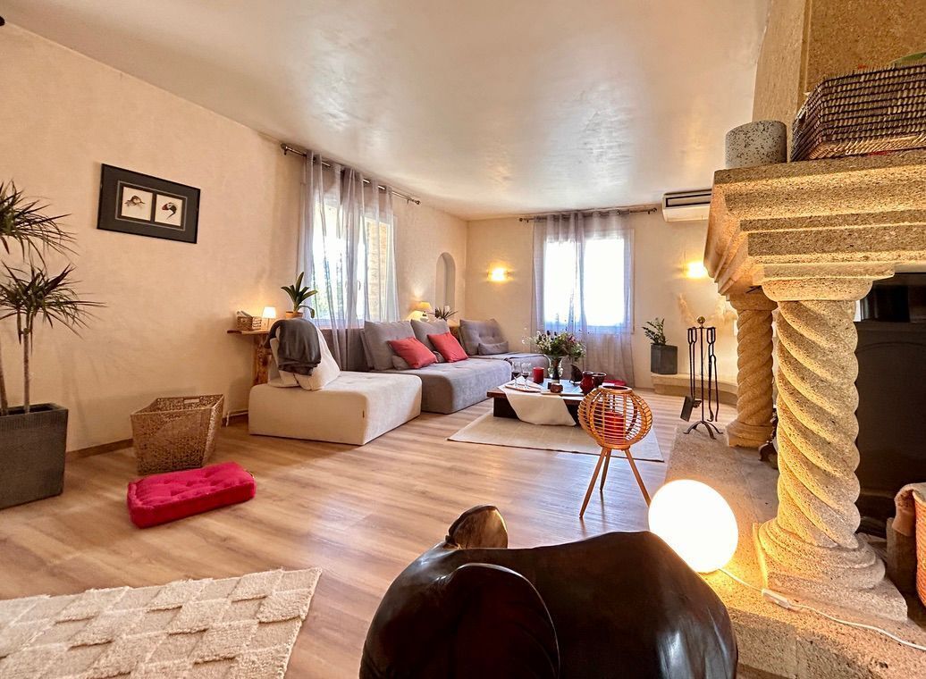 Ein Wohnzimmer mit einer Couch, einem Couchtisch, einem roten Hocker, einem Sessel und einer Steinsäule.