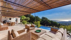 Ein überdachter Außenbereich mit Korbmöbeln, einem Pool und Blick auf das Meer.