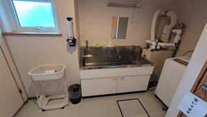 Une cuisine compacte équipée d’un évier en acier inoxydable, d’une petite poubelle, d’un panier à linge et d’une fenêtre.