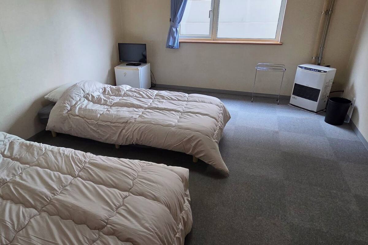 Quarto com duas camas, televisão sobre um pequeno móvel, aquecedor e janela com cortinas.