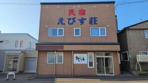 Un edificio de dos pisos con un letrero que dice '民宿 えびす荘' y otro letrero debajo que dice 'リゾート'.