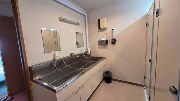 Une salle de bain avec un long lavabo, un miroir, un sèche-mains et une poubelle.
