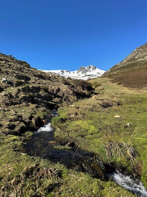 Een bergachtig landschap met een beek, rotsachtig terrein en besneeuwde toppen.