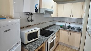Eine kleine Küche mit Kühlschrank, Mikrowelle, Herd, Spüle und Schränken.