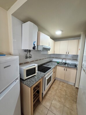 Cocina compacta con refrigerador, microondas, estufa, fregadero y gabinetes.