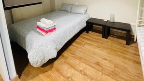 A small, single-bed room with a wooden floor, a grey bedspread, a bedside table, and a hanging lamp. - Mountain Ski Apartment in San Isidro Ski Resort (Puebla de Lillo)