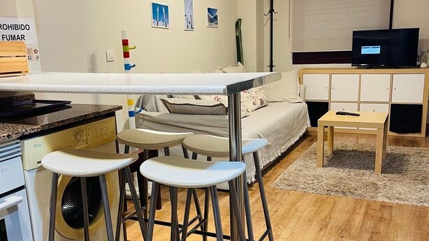 A modern kitchen with a central island, bar stools, a washing machine, and a dining area with a TV. - Mountain Ski Apartment in San Isidro Ski Resort (Puebla de Lillo)