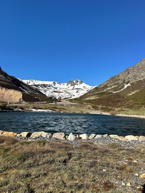 A mountain landscape with a lake, rocky shoreline, and a road leading to a building.
