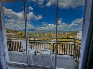 A balcony with two white chairs and a table, overlooking a mountainous landscape with scattered houses. - Red Chillies Nature Inn - Kandy (Kandy)