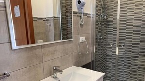 A bathroom with a white sink, a handheld hair dryer, and a glass-enclosed shower. - Locanda 115 (Realmonte)