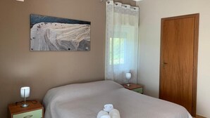 Une chambre d’hôtel avec un lit, une table de chevet avec une lampe, un tableau au mur, une fenêtre avec des rideaux et une porte en bois.