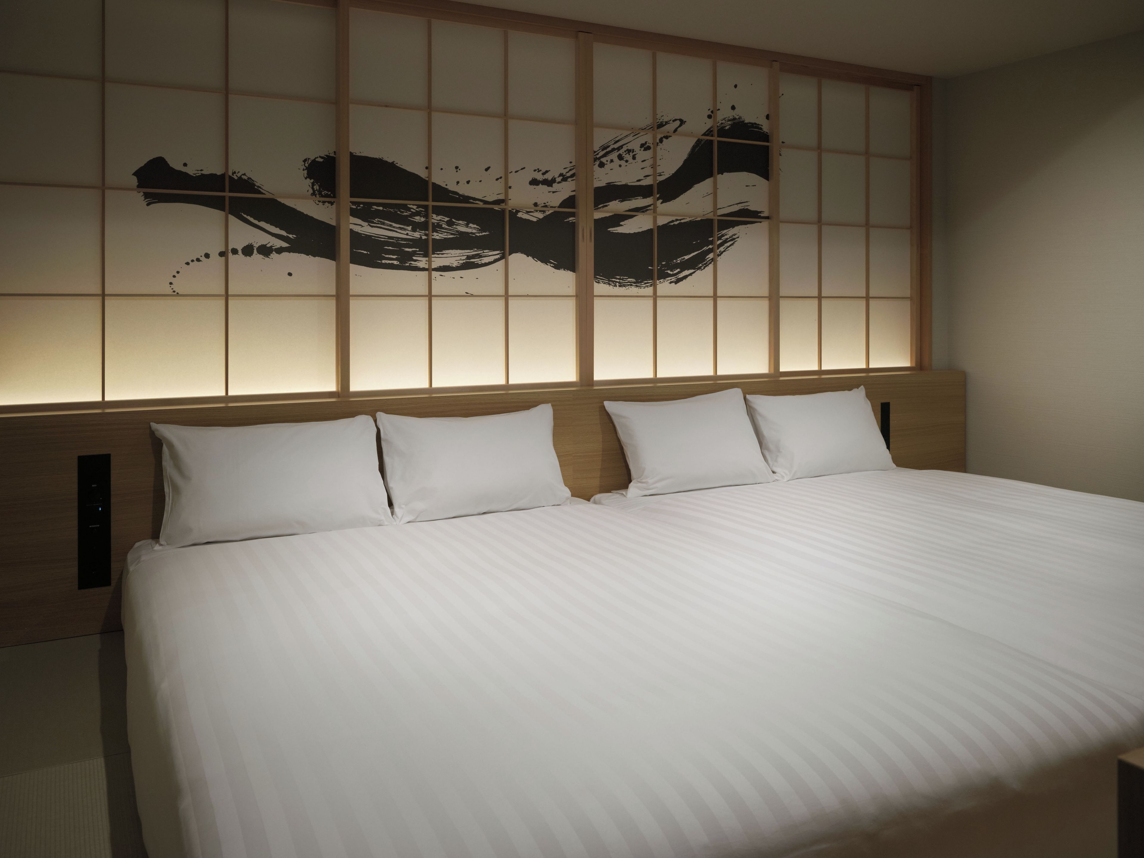 A hotel room with a large bed, a headboard with a light panel, and a wall with a black abstract design.