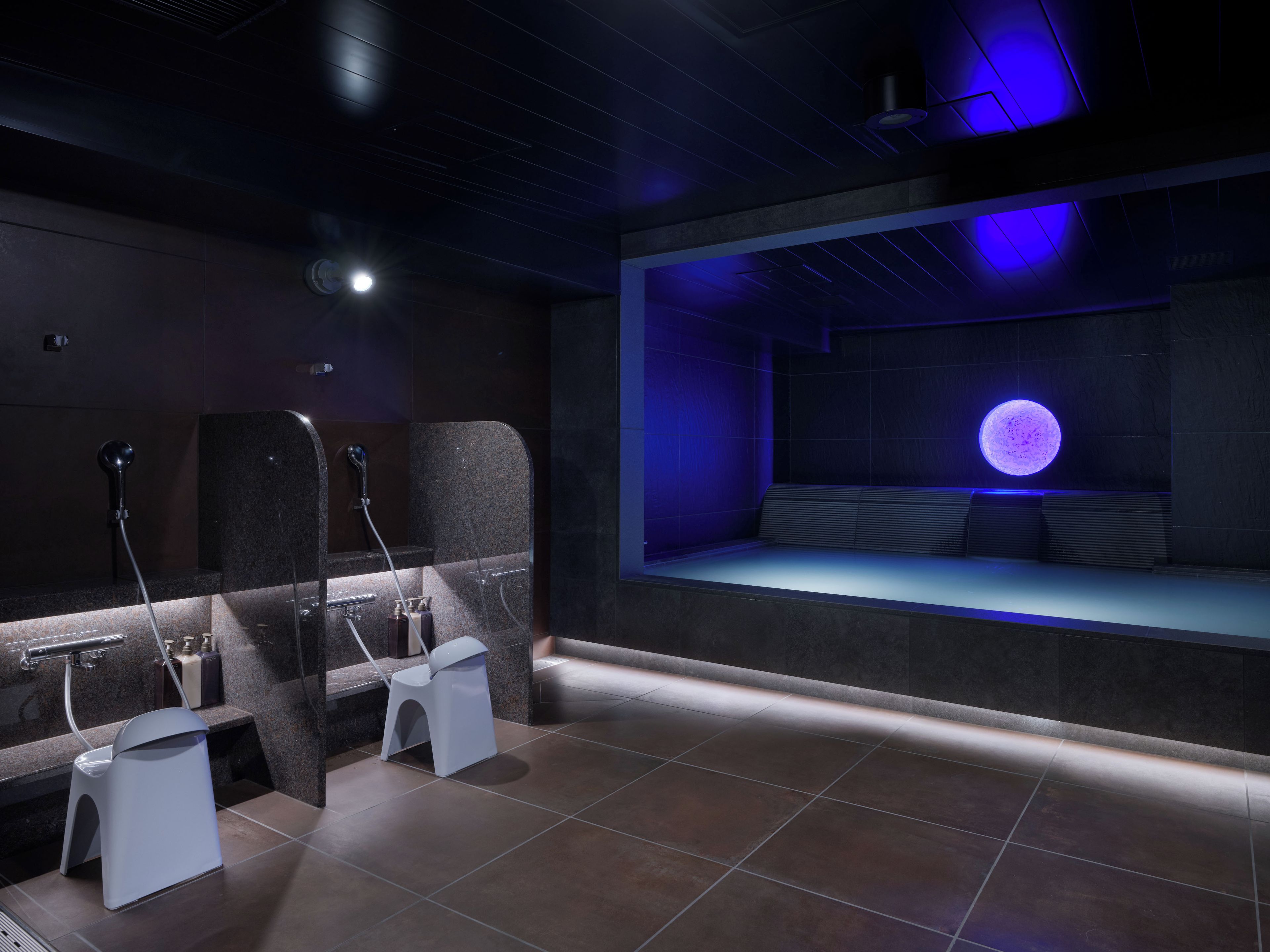 Ein moderner Spa-Raum mit einer großen, mondähnlichen Leuchte, einer Sitzecke und einer Dusche mit Duschbrause.