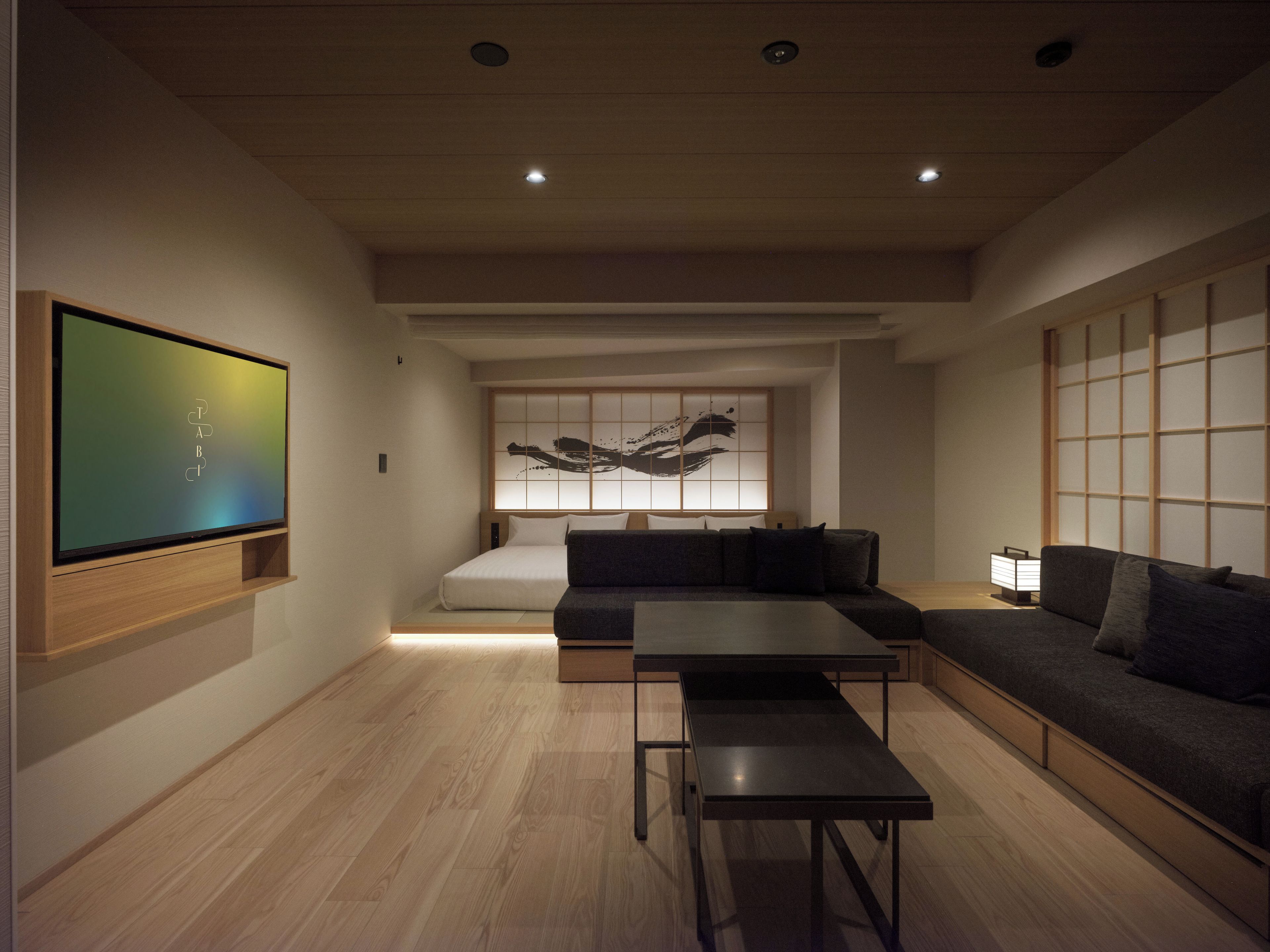 A modern living room with a flat-screen TV, a sofa, a coffee table, and a tatami mat wall.