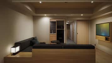 A modern hotel room with a sofa, a small table, a TV mounted on the wall, and a hallway leading to a bathroom.