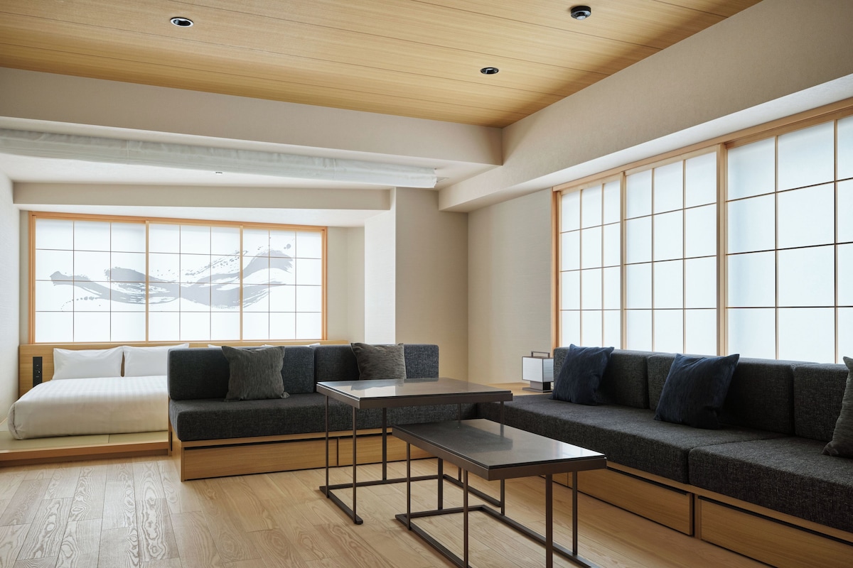 A modern hotel room with a sectional sofa, a small table, and a large window with a view.
