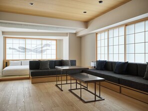 A modern hotel room with a sectional sofa, a small table, and a large window with a view. - TABI ASAKUSA (Tokyo)