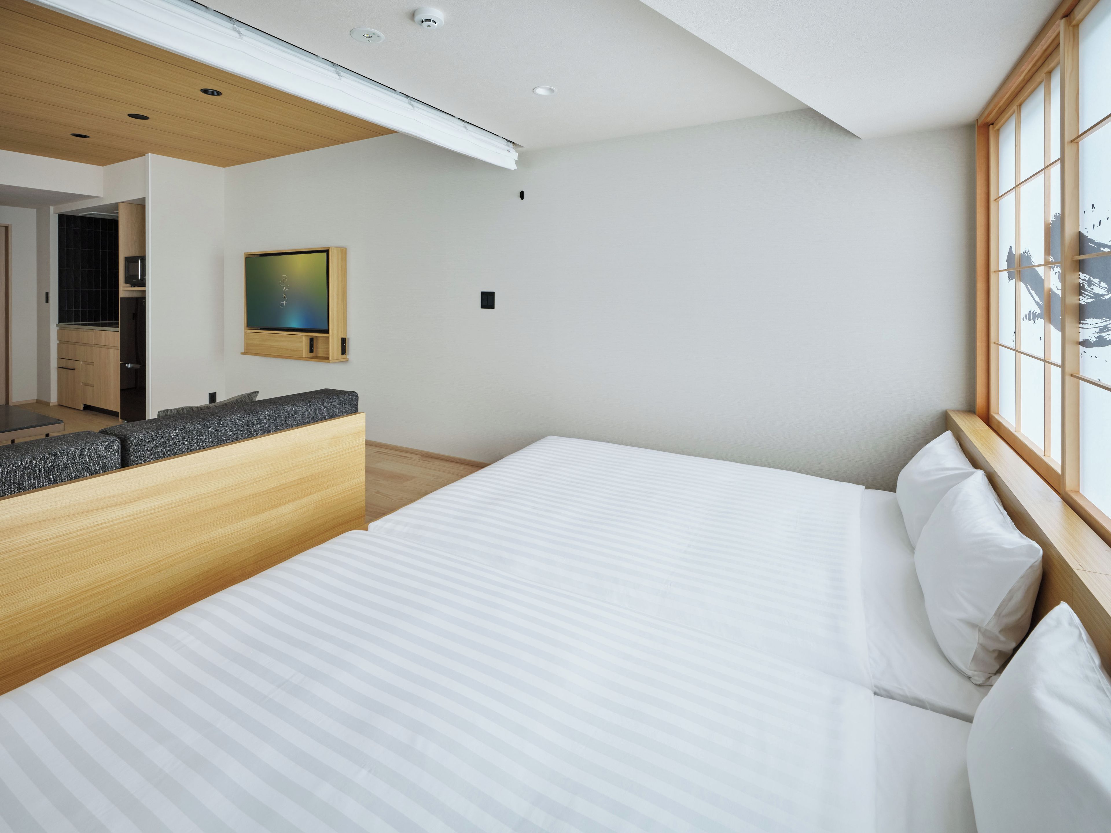 A modern bedroom with a large bed, a wooden bench, and a view of a mountain through a window.