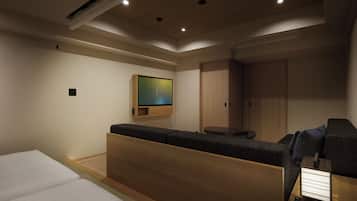 A modern hotel room with a bed, a seating area, a TV mounted on the wall, and a wardrobe.