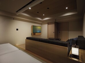 A modern hotel room with a bed, a seating area, a TV mounted on the wall, and a wardrobe.