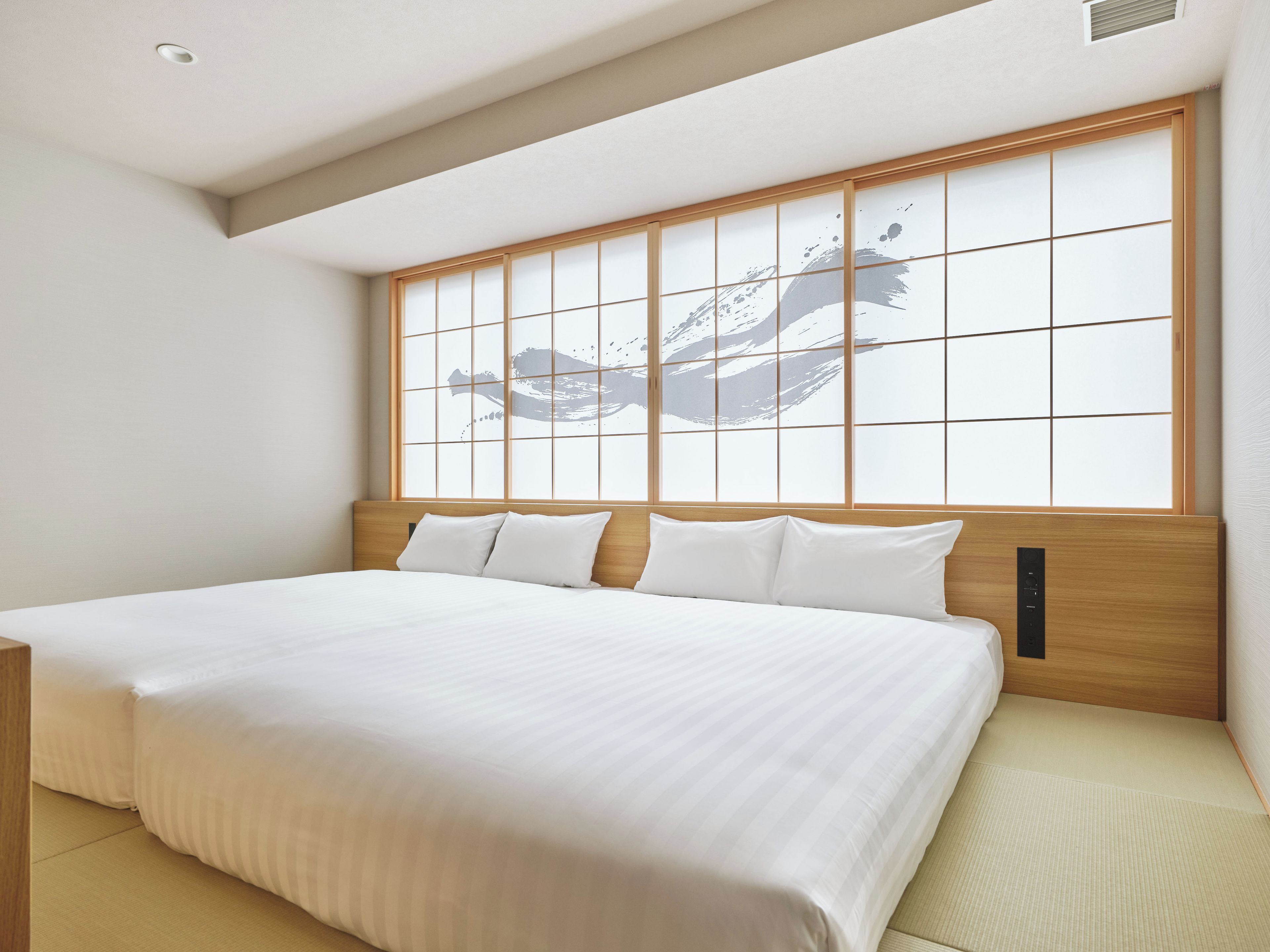 A neatly made bed with a wooden headboard and a large window with a traditional Japanese design.
