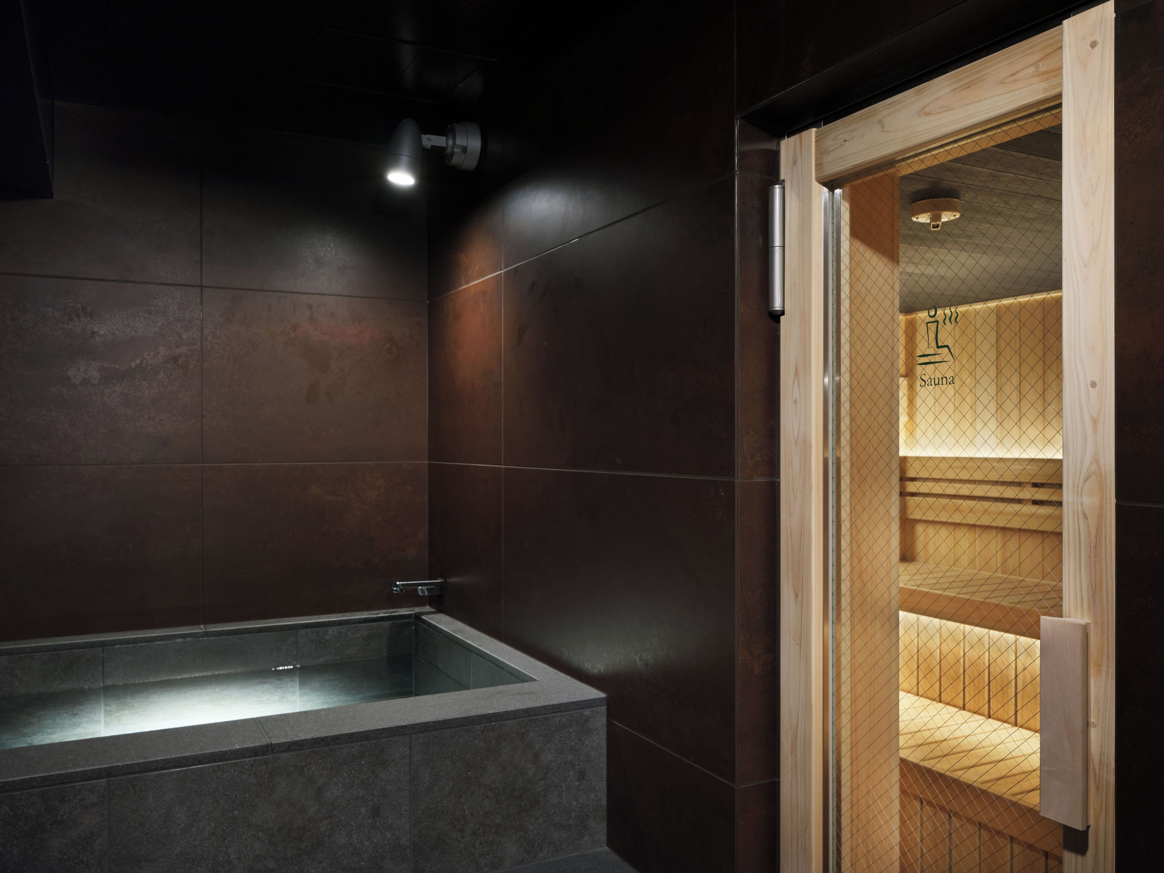 A modern bathroom with a freestanding bathtub, wooden sauna, and a visible sauna sign.