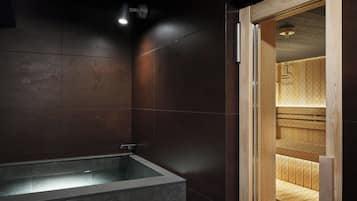 A modern bathroom with a freestanding bathtub, wooden sauna, and a visible sauna sign.