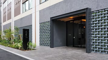 A modern building entrance with a dark facade, a metal gate, and a small garden area with plants.