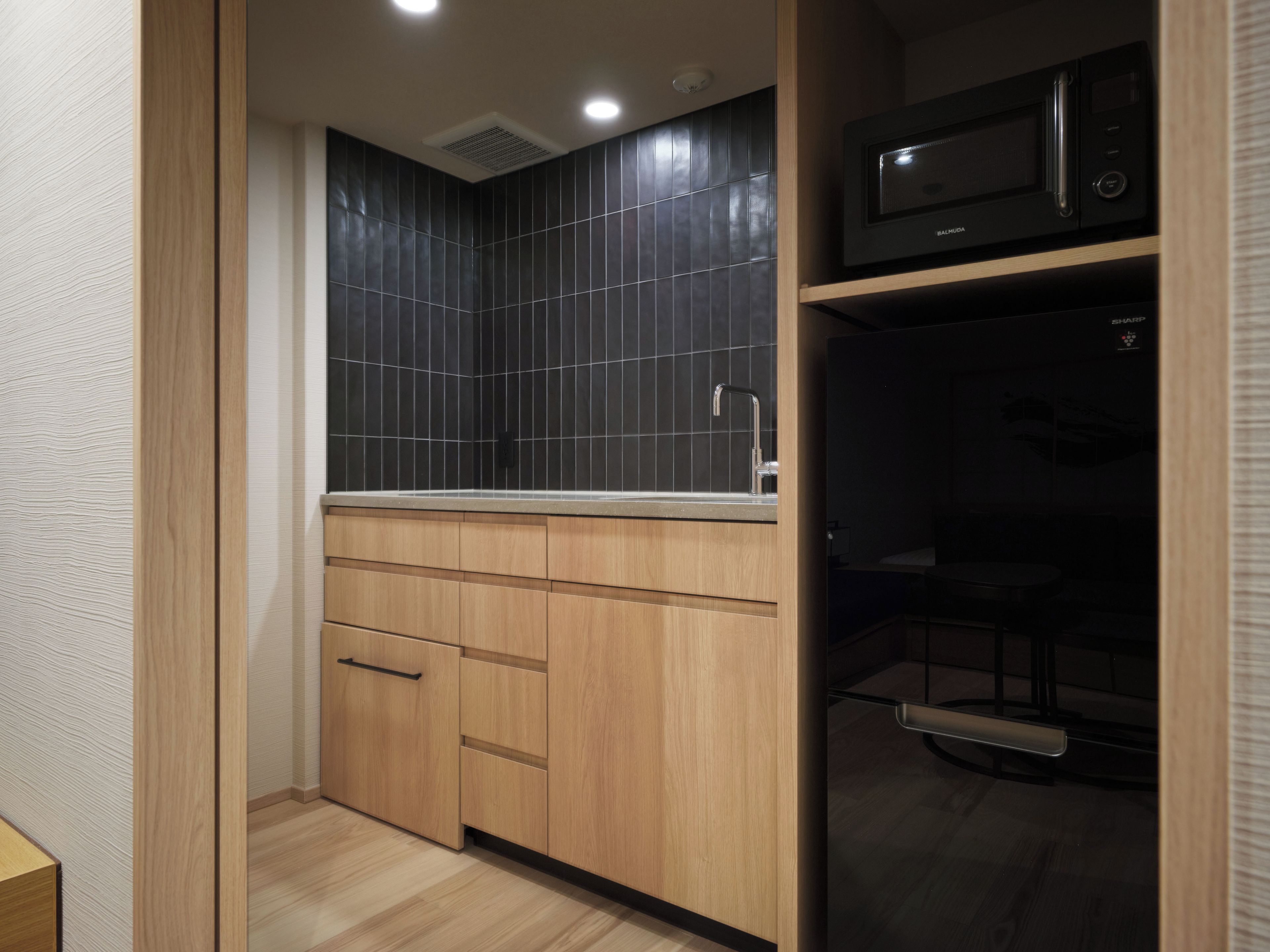 A modern kitchen with dark tiles, wooden cabinets, and a microwave.