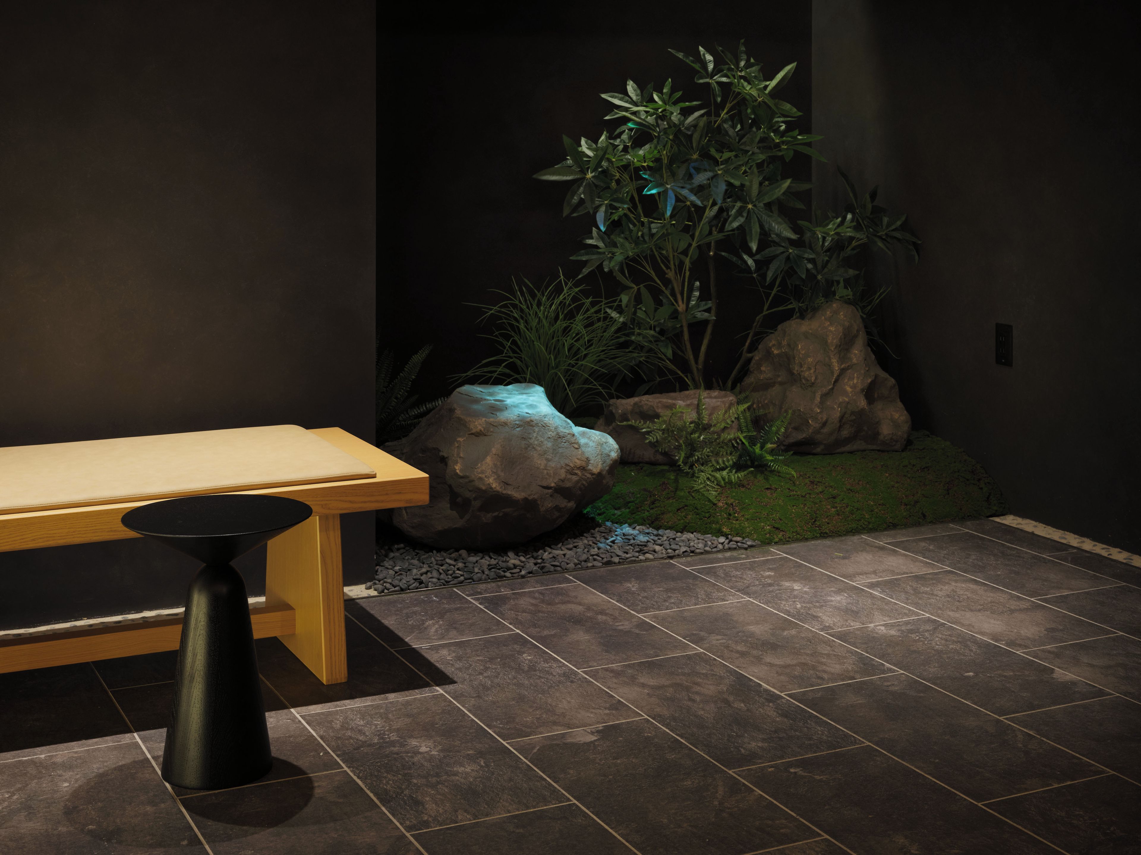 Un intérieur moderne agrémenté d’un banc en bois, d’une table en pierre et d’un jardin de rocaille avec des plantes.