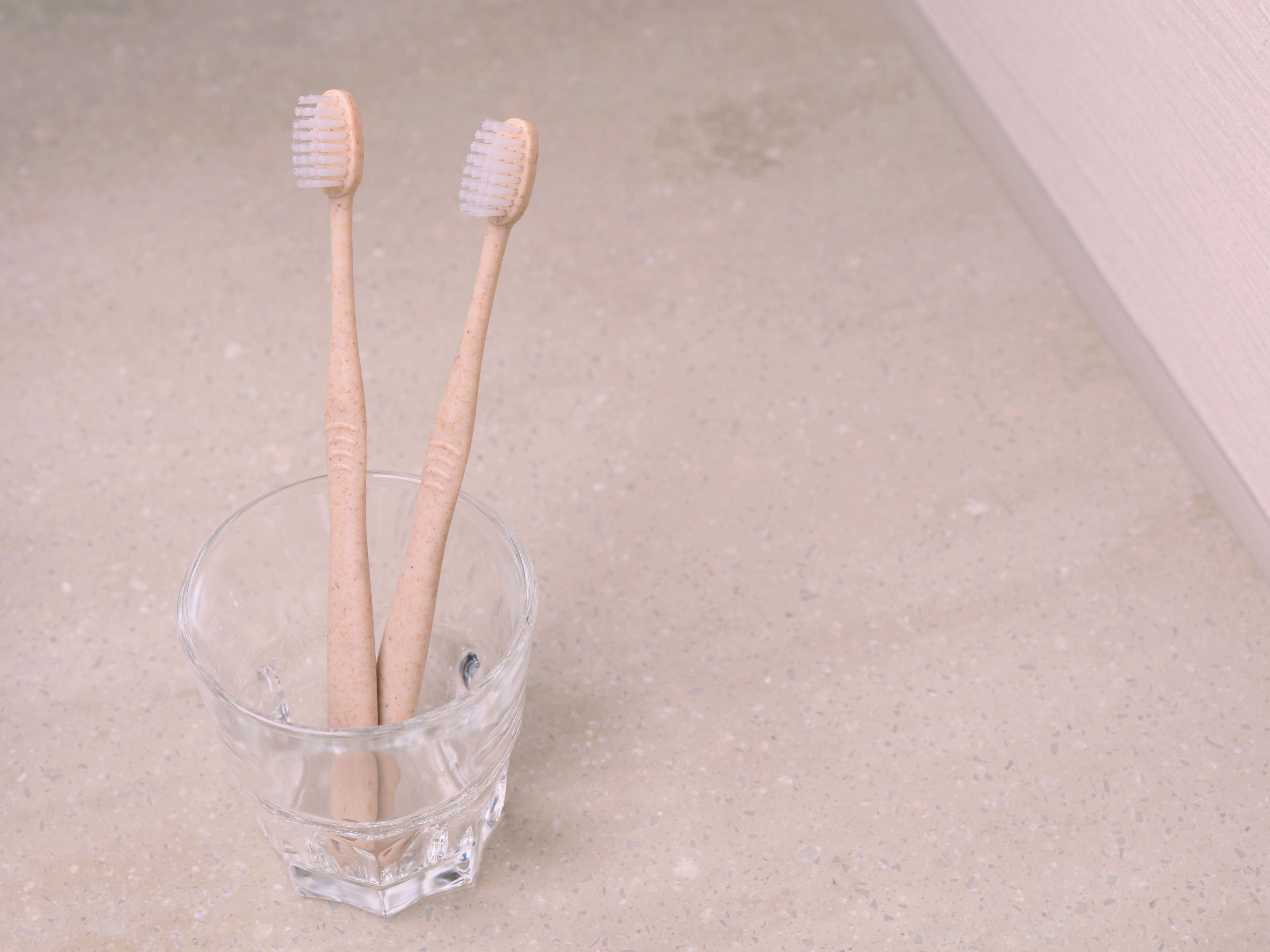 Two toothbrushes in a clear glass cup on a countertop.
