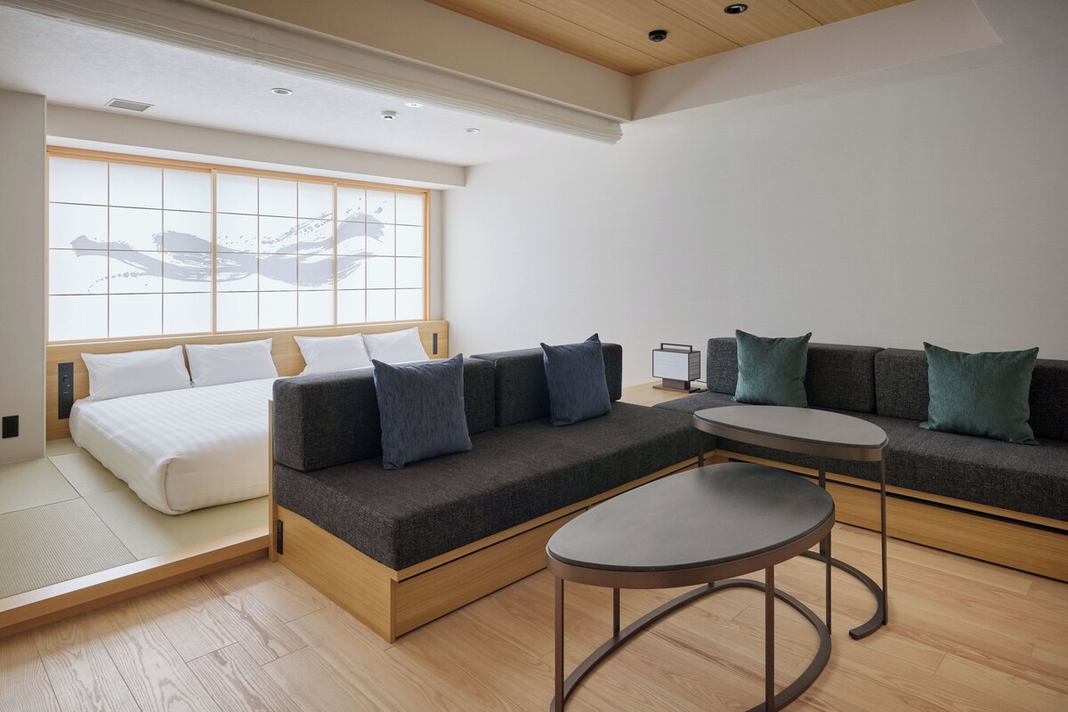 A modern hotel room with a bed, sofa, and round table.