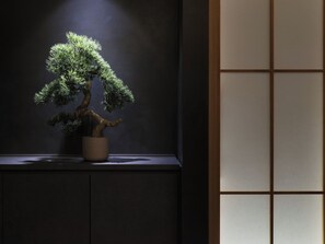 A bonsai tree in a pot on a dark surface with a wooden panel in the background. - TABI ASAKUSA (Tokyo)