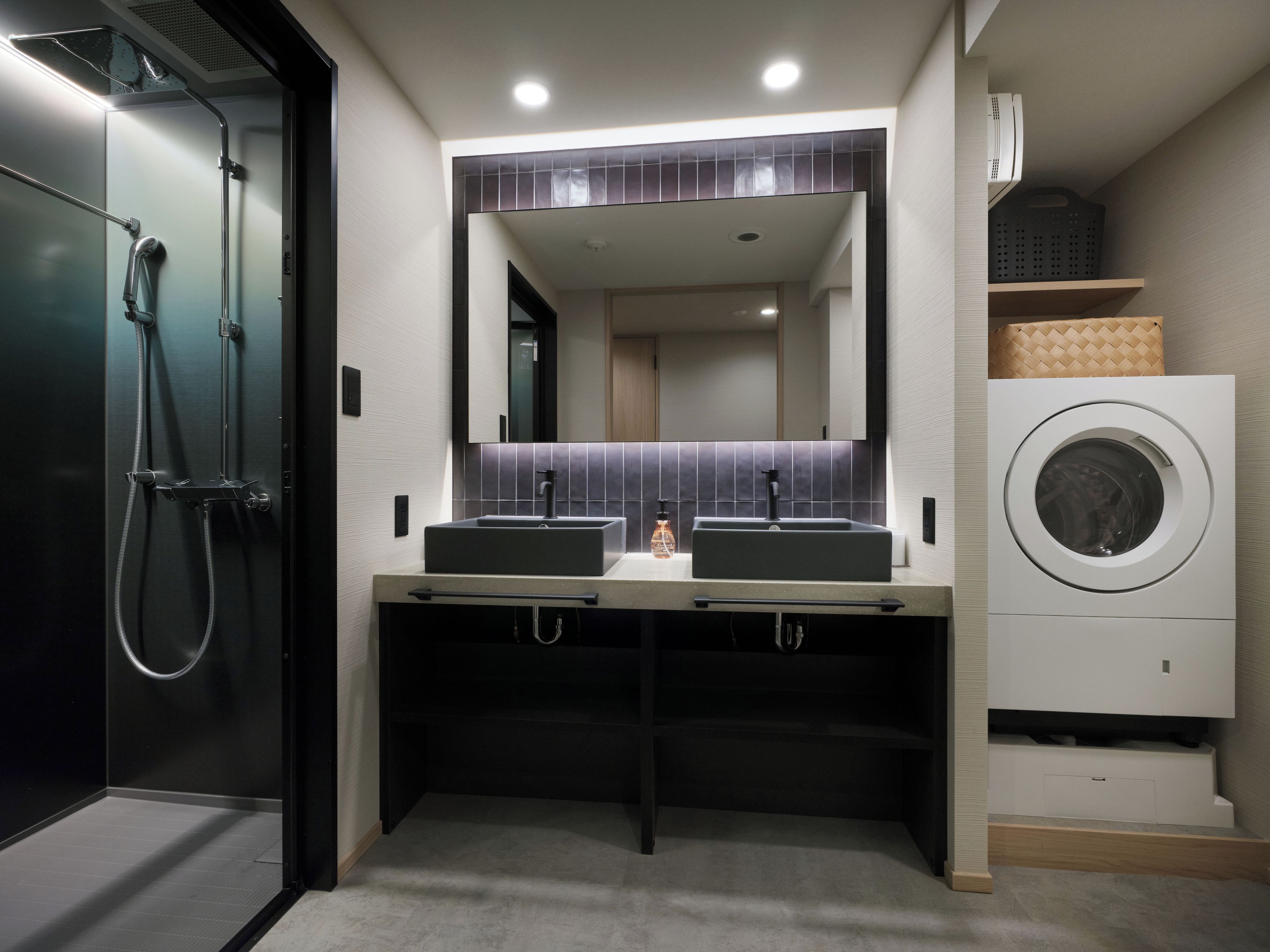 A modern bathroom with a double sink, a mirror, a shower, and a built-in washing machine.