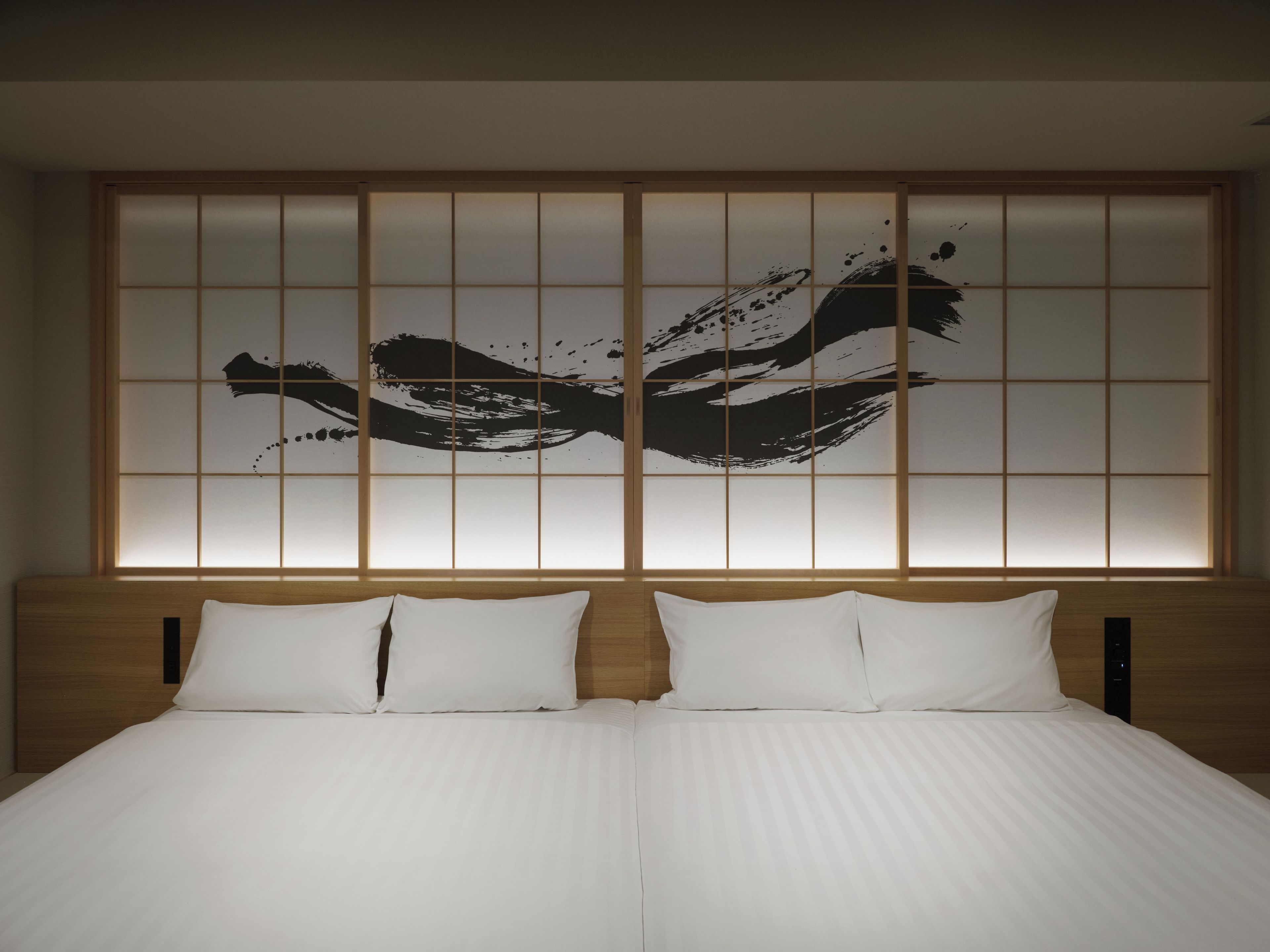 A hotel room with a large bed, two pillows, and a wall with a black abstract design.