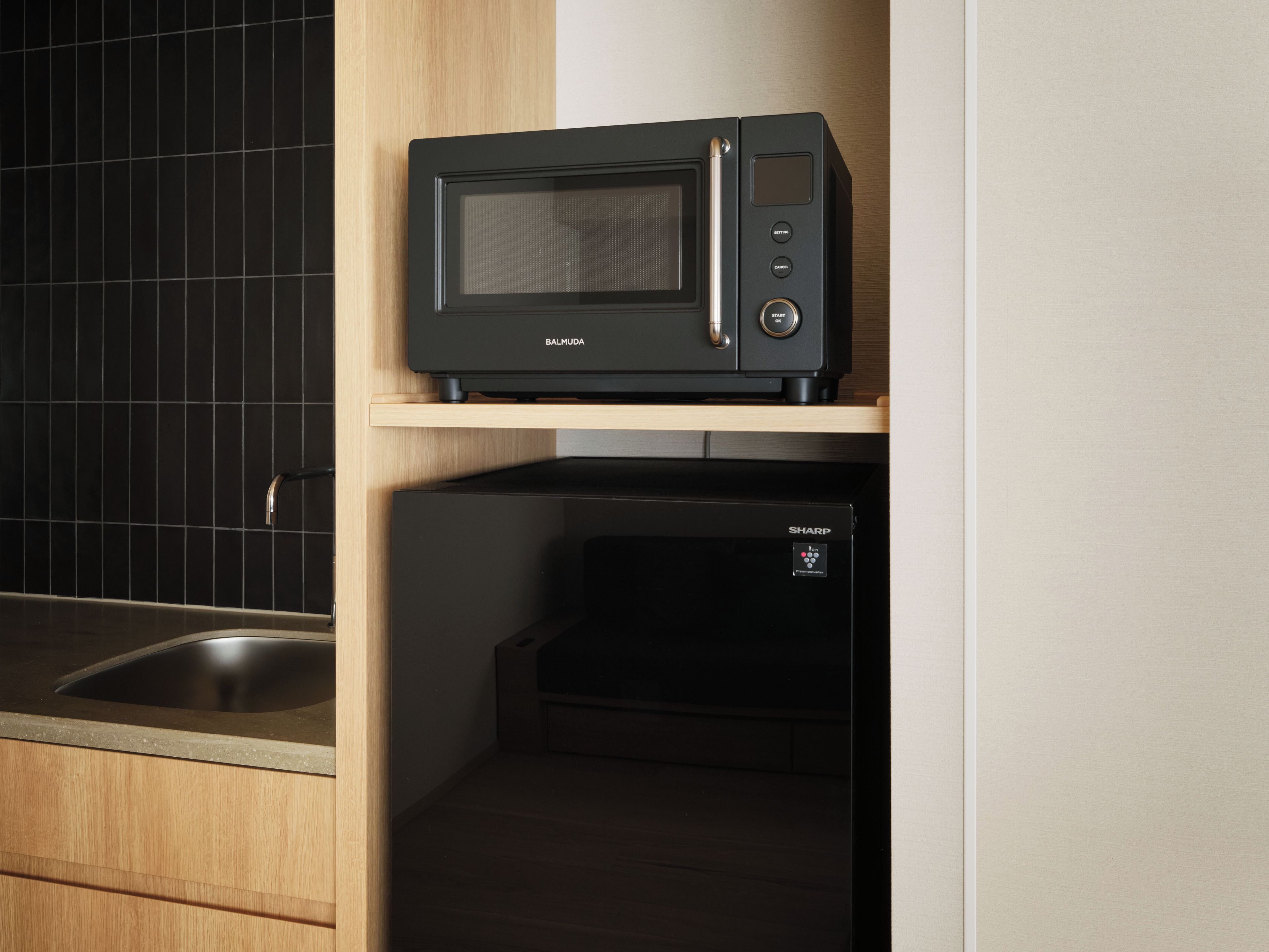 Una cucina con un forno a microonde nero su uno scaffale, una lavastoviglie nera sotto e uno schienale rivestito in piastrelle.