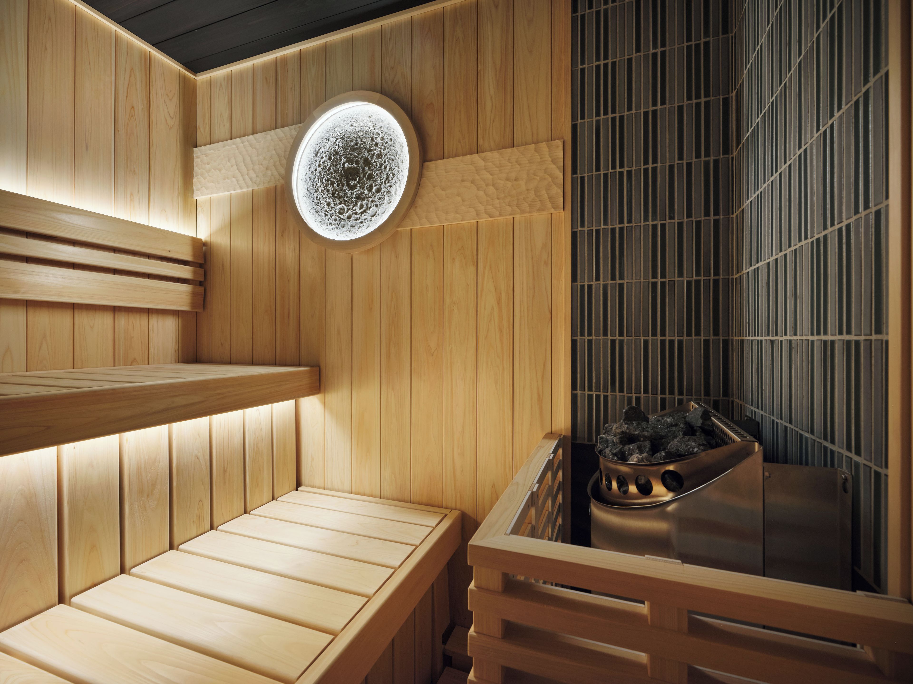 Een sauna met houten banken, een ronde lamp en een stenen wasbak.
