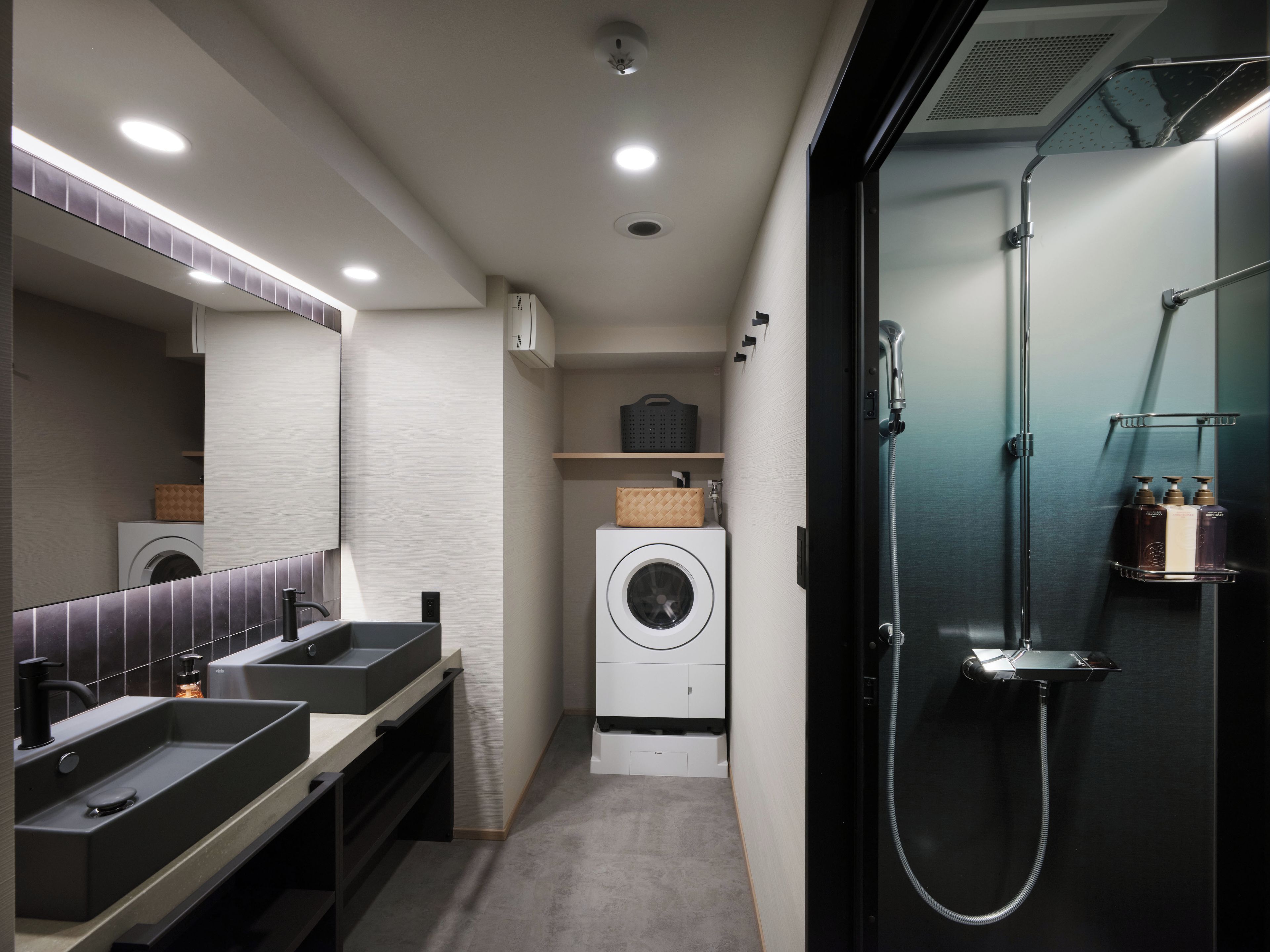 A modern bathroom with dual sinks, a large mirror, a washing machine, and a shower enclosure.