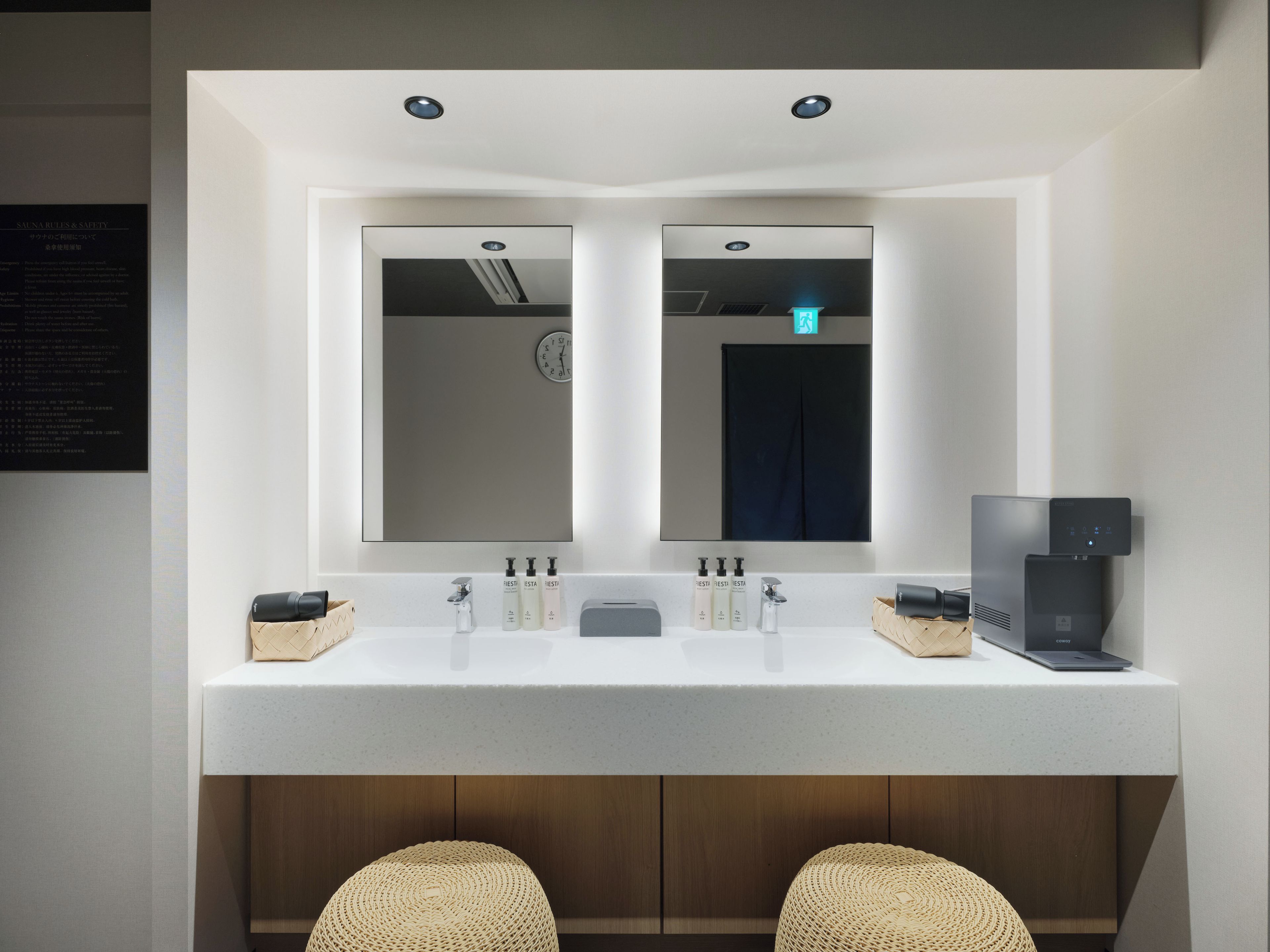 Une salle de bain moderne avec un meuble-lavabo à deux vasques, un miroir, une horloge et une machine à café.