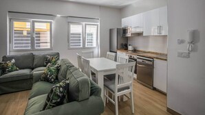 Un appartement moderne comprenant un espace de vie, une table à manger, des chaises blanches, une cuisine avec des meubles blancs et un four encastré.